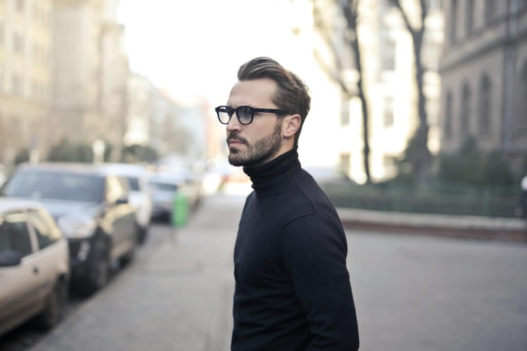 pexels-photo-839011-839011 A fashionable man in a black top and glasses poses in an urban street with parked cars.